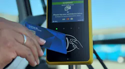 A hand taps a Chase Sapphire credit card on a yellow open-payment fare reader displaying ‘In Service, Please tap your card/device below.