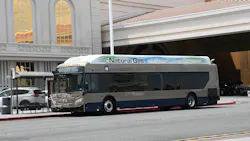 An RTC of Southern Nevada bus, unit 17615, in tan and navy livery with “Powered by Natural Gas: The cleaner, greener way to go” on its roof panel, displays “117 To South Strip Transfer Terminal” while stopped at a curb beside a large resort building.