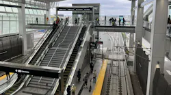 An elevated LAX/Metro Transit Center station, with escalators and stairs leading down to a light rail platform where riders wait, tracks visible below.