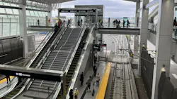 An elevated LAX/Metro Transit Center station, with escalators and stairs leading down to a light rail platform where riders wait, tracks visible below.