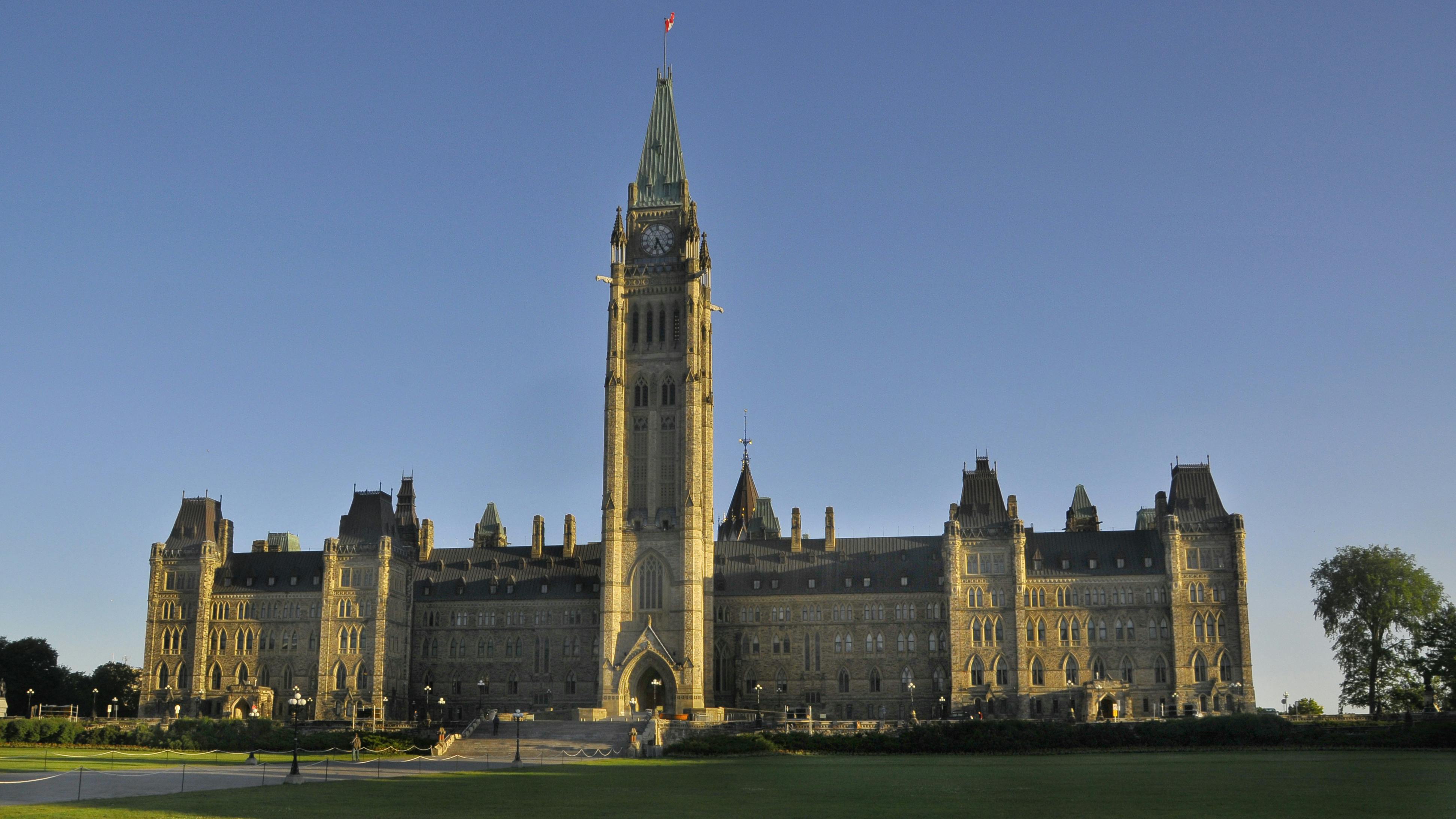 Canada&rsquo;s Parliament Hill Centre Block and Peace Tower under a clear blue sky, viewed from the lawn.