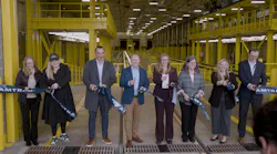 Eight people cut an Amtrak ribbon together inside a yellow-painted train maintenance facility in Seattle.