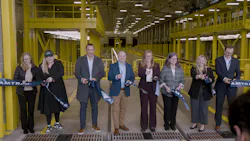 Eight people cut an Amtrak ribbon together inside a yellow-painted train maintenance facility in Seattle.