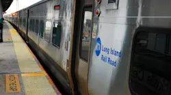 A Long Island Rail Road train stopped at a station platform, with its door open beside a ‘Watch the Gap’ warning strip.