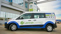 A white, blue and green Lextran Connect on-demand van, unit 1224, with “By Via” and “Lexington” branding, is parked in front of a gray Lextran facility with a recruiting sign reading “Next stop? Lextran!”